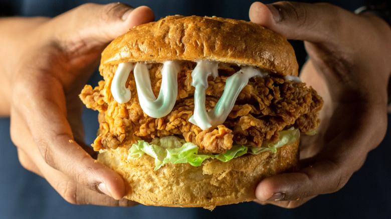 Hands holding a crispy fried chicken burger with lettuce