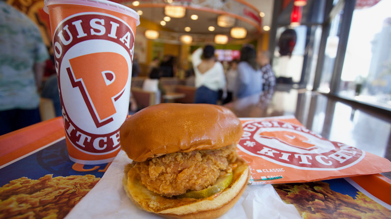 A Popeyes fried chicken sandwich sits on a restaurant tray with a soda adjacent