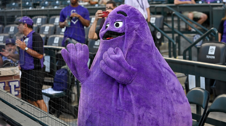 McDonald's fuzzy purple mascot Grimace stands behind the netting at a baseball game