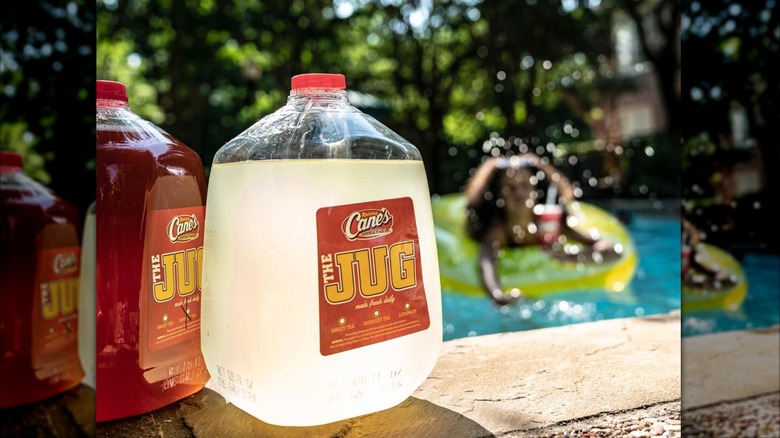 Jugs of Raising Cane's tea and lemonade are pictured in an outdoor setting, with people swimming in a pool in the background