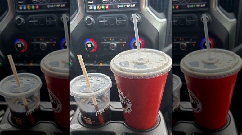 A large Panda Express cup sits next to a McDonald's in a driver's console, dwarfing the McDonald's soda