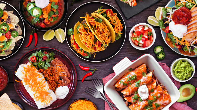 A variety of different Mexican dishes on a table, including tacos, burritos, enchiladas, and guacamole