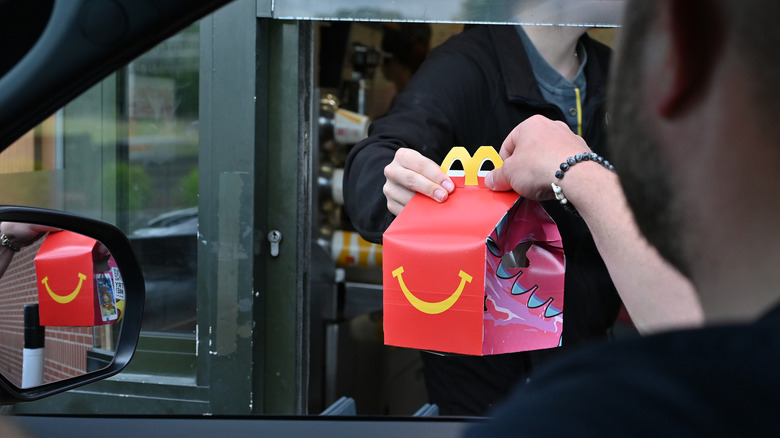 A person grabs a Happy Meal from a McDonald's drive-through window