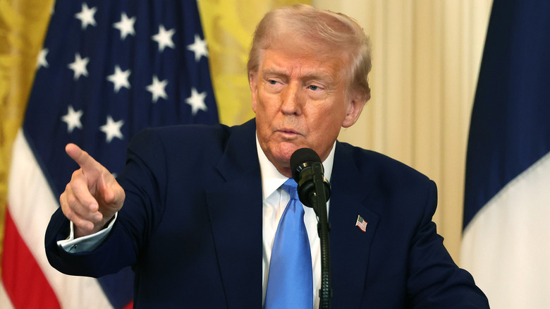 U.S. President Donald Trump points while speaking into a mic in front of the U.S. flag
