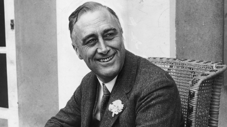 Black and white portrait of U.S. President Franklin D. Roosevelt smiling at a desk