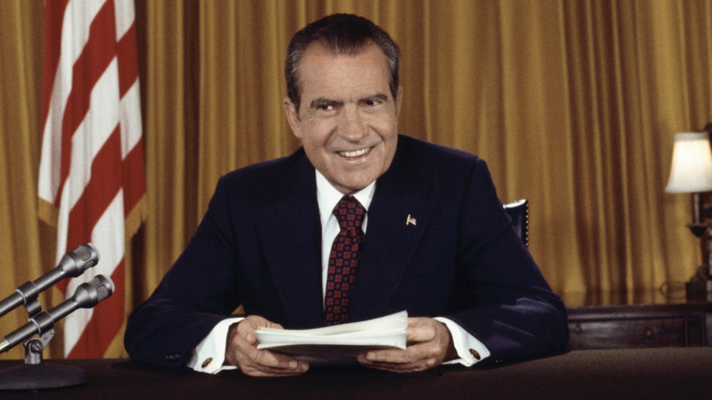 U.S. President Richard Nixon sits at a desk holding papers near a mic