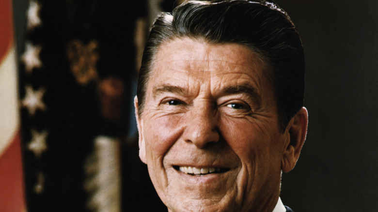 U.S. President Ronald Reagan smiles in front of a U.S. flag