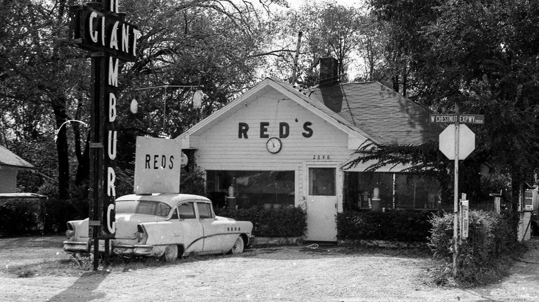 Black and white photo of front of Red's Giant Hamburg restaurant, with a car and sign out front.