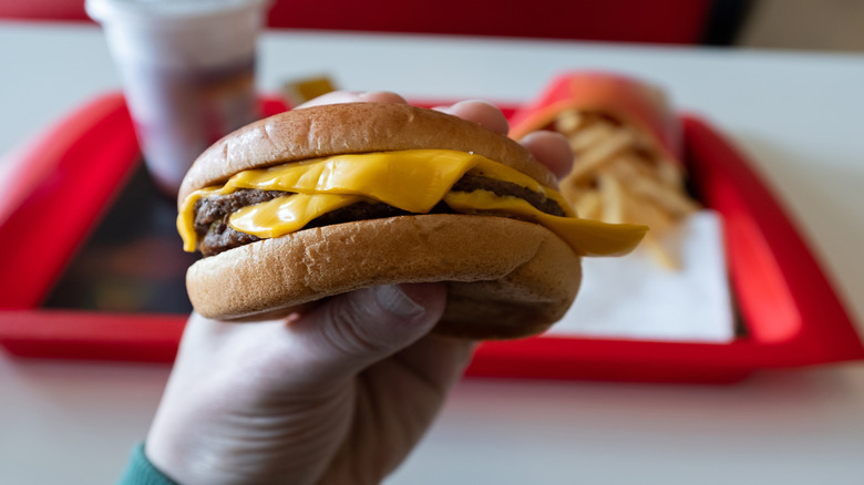 A double cheeseburger is held by a customer at a fast food restaurant