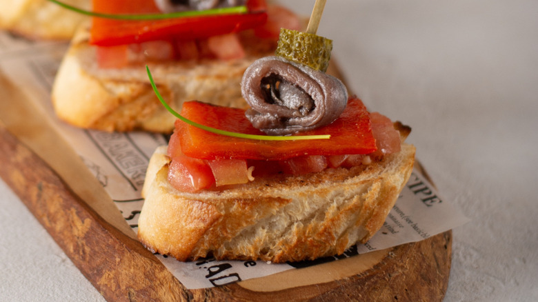 Tapa of bread topped with tomato and a rolled anchovy