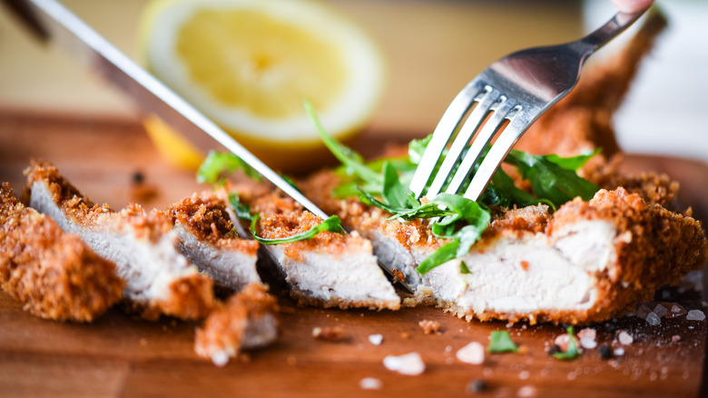 Pork schnitzel being sliced with fork and knife