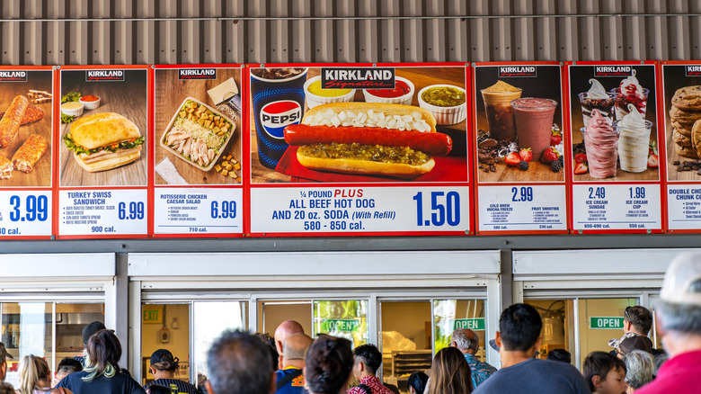 Many members wait in line to order at the Costco food court, with menu items displayed above their heads