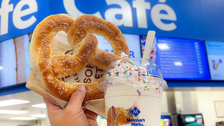 A sam's club shopper holds up a half-salt, half cinnamon soft pretzel and an ice cream sundae inside a Sam's club cafe