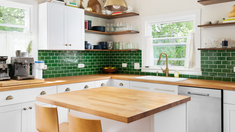 A sunny, green-tiled kitchen with an apron sink, brass fixtures, and a wooden kitchen island