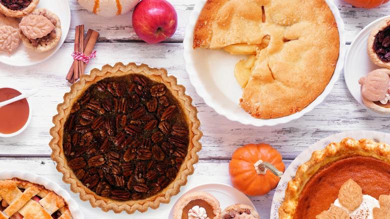 A table filled with lots of different pies, Fall spices, pumpkins, and apples