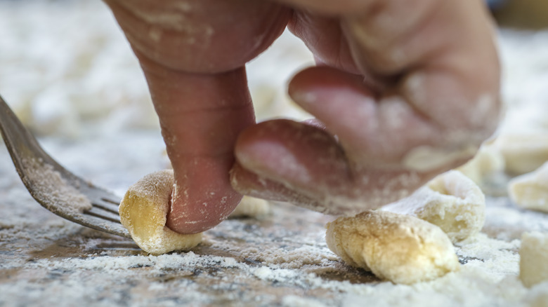 Hand pressing gnocchi against a fork