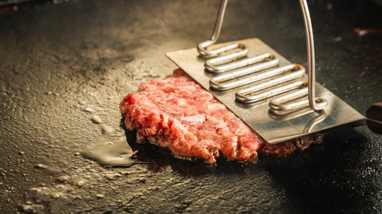 A burger patty gets smashed on a griddle