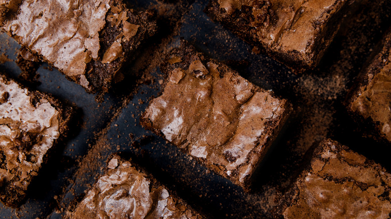 Brownies, cut into neat rectangles, that have crinkly tops, sit on a black stone countertop