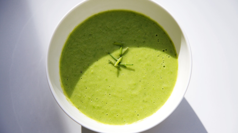 A bowl vibrant green pea soup against a white background.