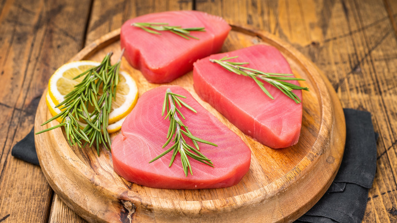 Three raw ahi tuna steaks on wooden cutting board with lemon and rosemary