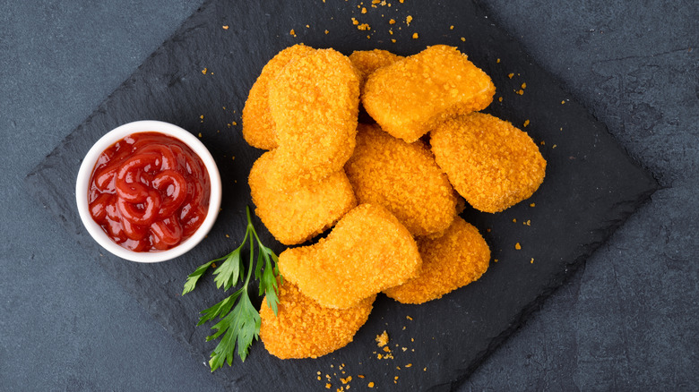 Pile of breaded chicken nuggets with small bowl of ketchup