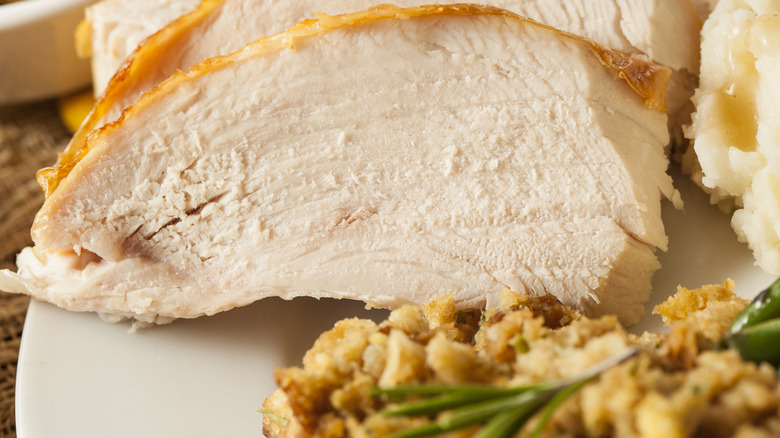 Sliced turkey next to mashed potatoes and gravy, green beans, and stuffing on a white plate.