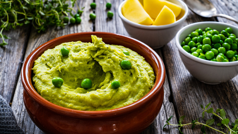 Pureed peas in mash sit next to a bowl of fresh pea sand lemon wedges