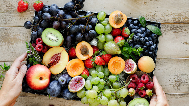 A person holding a box containing a variety of fruits.