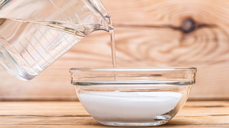 someone pours water into a bowl of baking soda, ready to soak something