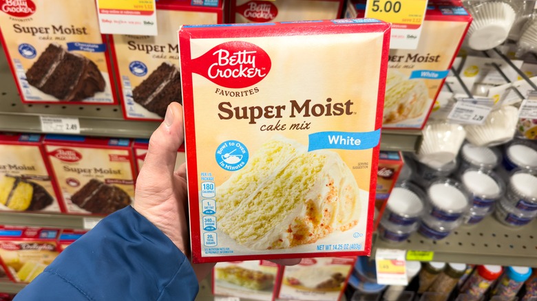Hand holding up boxed cake mix in the baking aisle of a grocery store