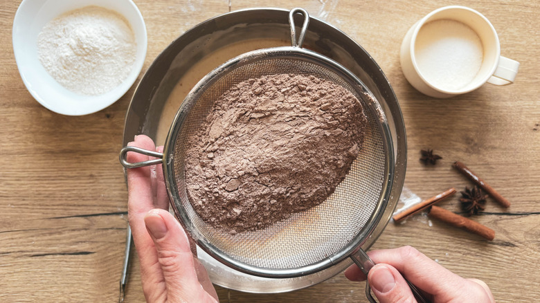Hands sifting a dry chocolate mixture into a bowl for baking