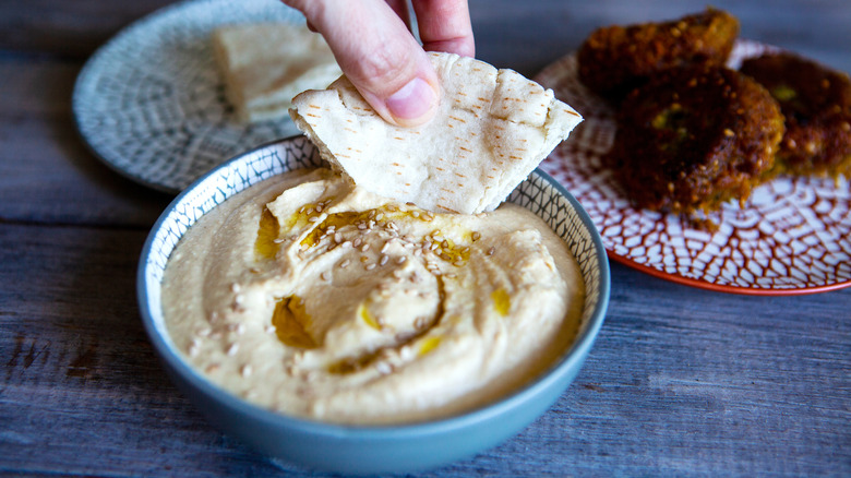 Handing dipping pita into bowl of hummus