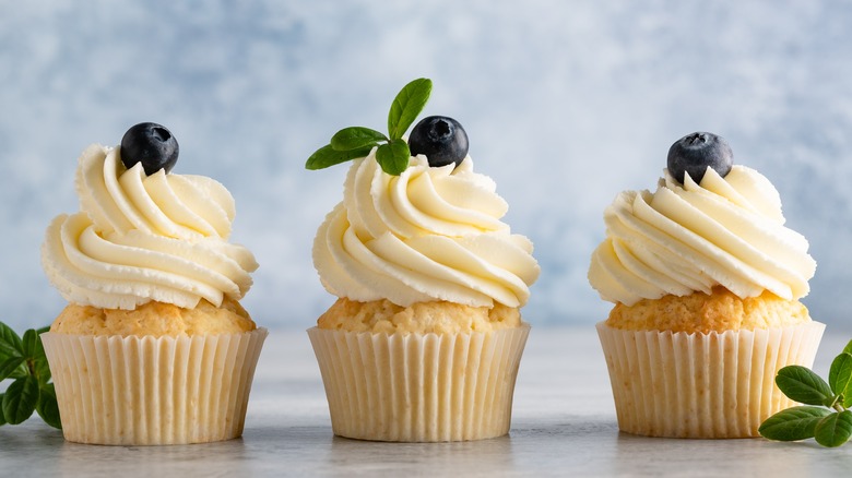Three vanilla cupcakes decorated with icing and blueberries