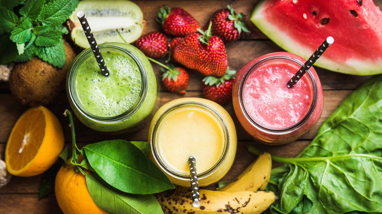 Green, yellow, and red smoothies surrounded by produce