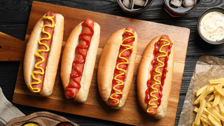 Four hot dogs with mustard and ketchup on a serving board
