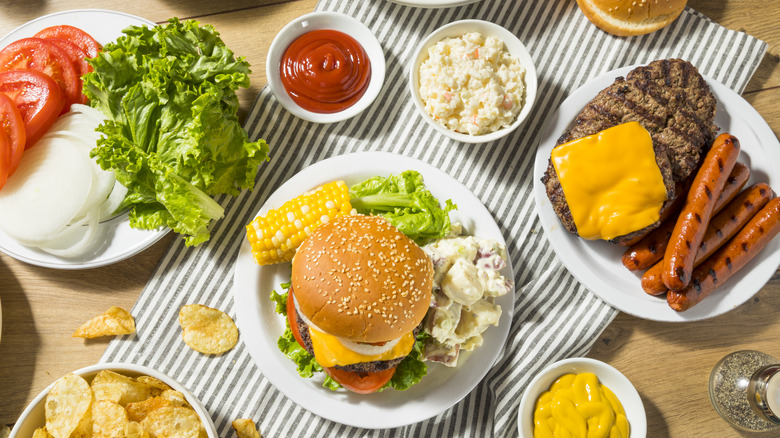 Burgers on a table with condiments, chips, and hot dogs