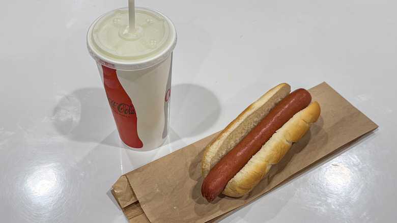 A Costco hot dog sits next to a refillable Coca-Cola soda.