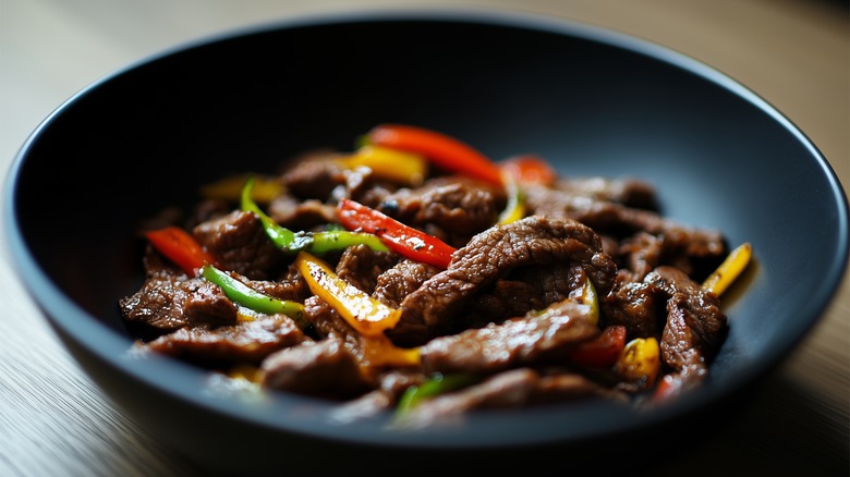 Black bowl of pepper steak stir fry on a wooden table