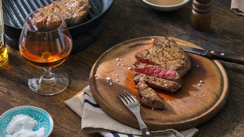 A grilled steak sits sliced next to a glass of whisky.