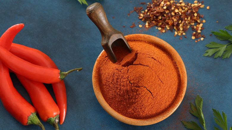 Cayenne chiles next to a bowl of cayenne powder, a scoop inside it.
