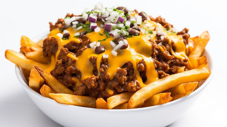 a bowl of chili cheese fries, topped with fresh red onion and cilantro