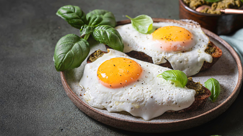 Fried eggs with pesto, cracked pepper, and basil are served on toast.