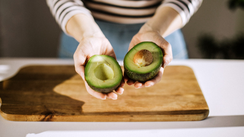 Person holding two halves of an avocado