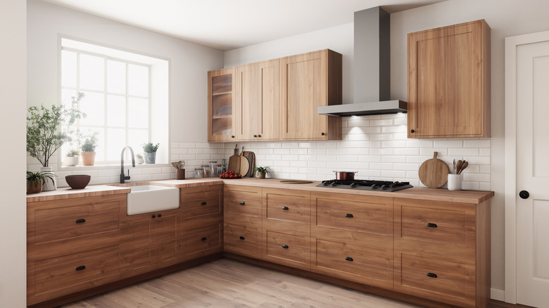 A kitchen with wooden floors and matching cabinets has a bright beam of sun coming in