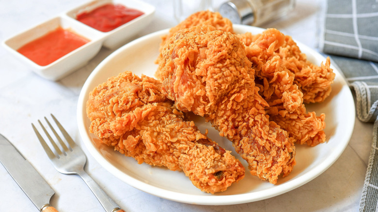 fried chicken on a white plate with dipping sauces and cutlery beside it