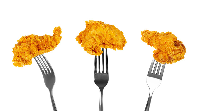 A row of fried-chicken-topped forks on a white background