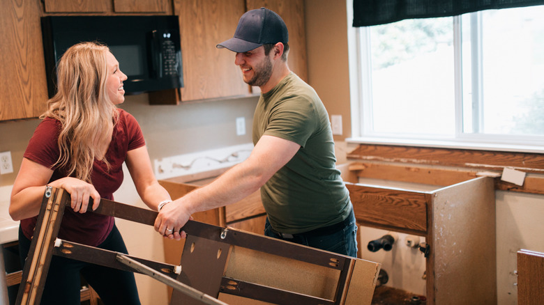 Two home owners move a piece of demolished cabinetry in an under-renovation kitchen space