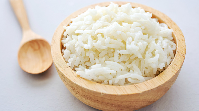 a wooden bowl full of steamed white rice with a wooden spoon to the lefthand side