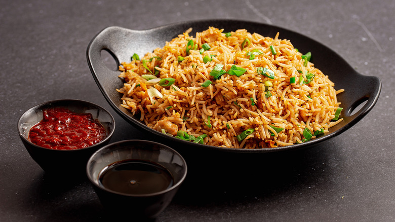 fried rice with chopped green onions in oval black bowl next to two dipping sauces, chili oil and black vinegar