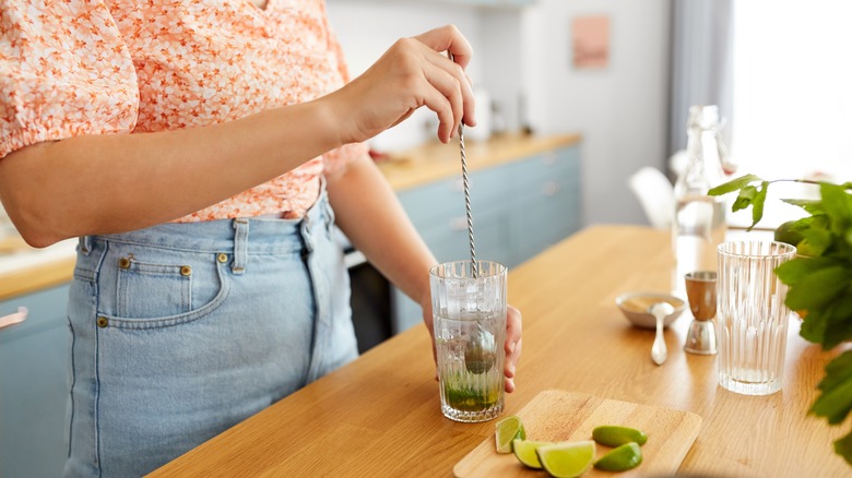 Woman stirring clear glass with ice and limes